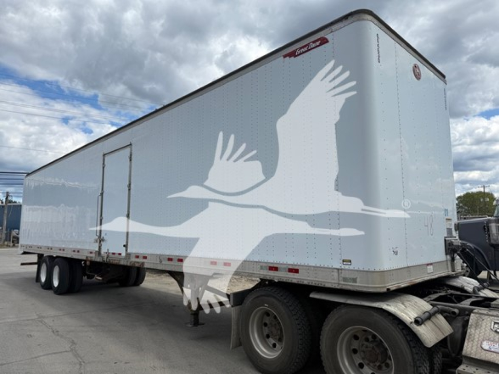 Great Dane van trailer with side door and two rear axles showing a large white bird graphic on light gray exterior.