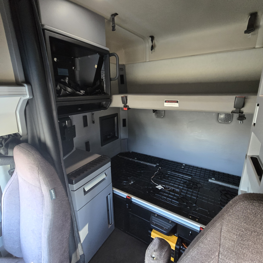 Truck sleeper cab interior showing storage shelf, control panel, and empty cargo area with black floor mat in a Mack Anthem truck.