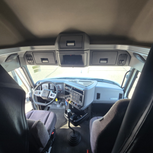 Truck cab interior view of a 2020 Mack Anthem showing steering wheel, dashboard, gear shifter, and overhead compartments.