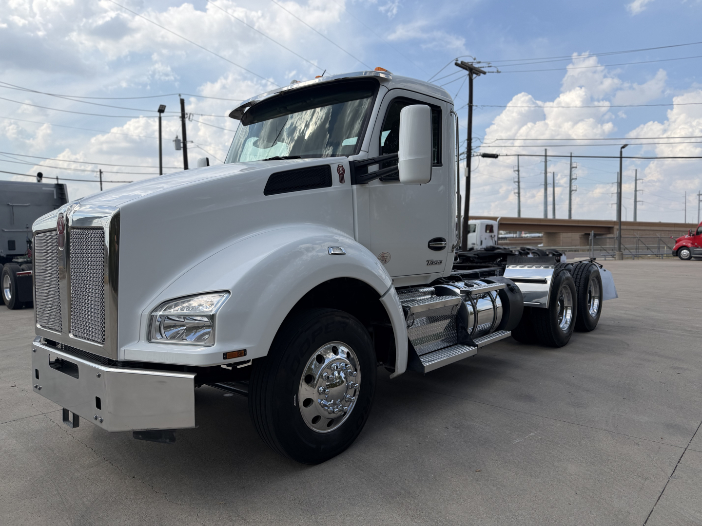 Kenworth T880 conventional daycab truck side view showing chrome front bumper, dual rear axles, white cab, and fuel tanks.