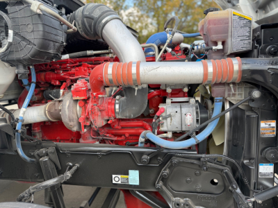 Kenworth T880 engine bay showing red diesel engine with blue and orange hoses, radiator cap, and labeling stickers.