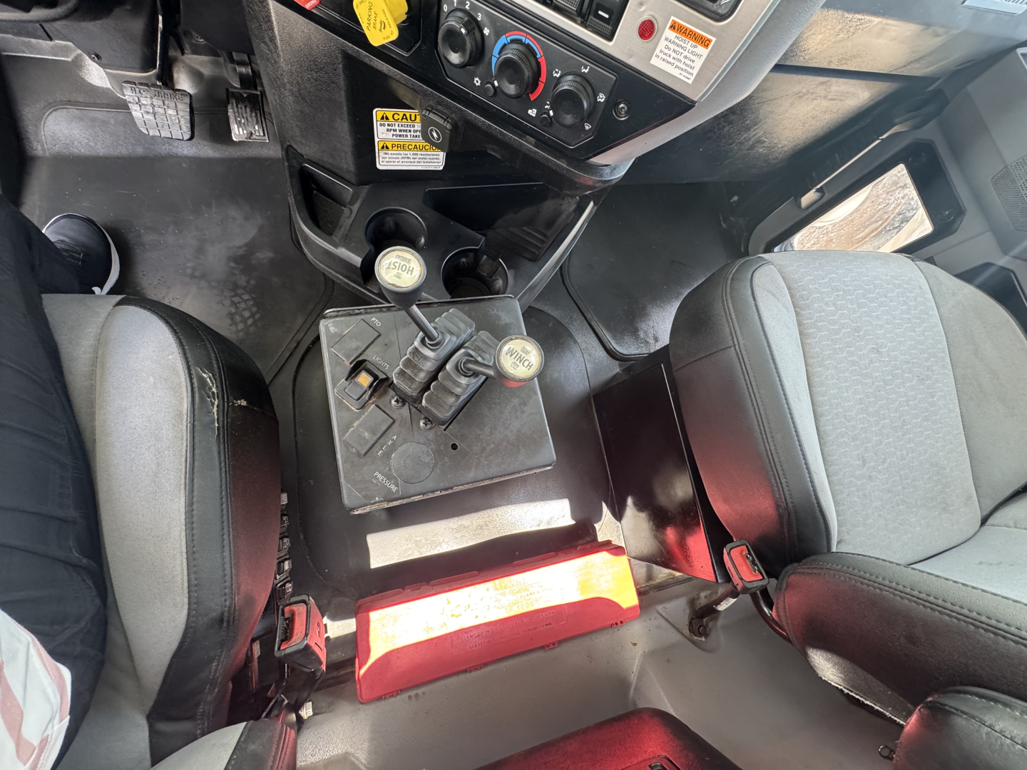Cab interior of a Mack GR64B rolloff truck showing two gear levers, center console, and seats.