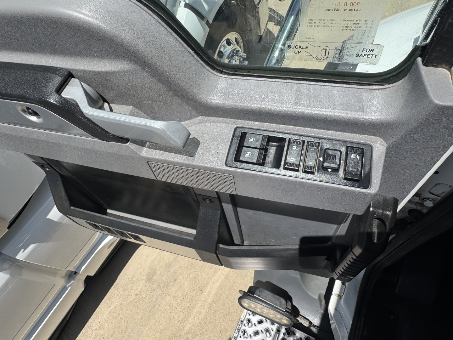 Dashboard view of a Mack truck cab showing control switches and window panel. Text visible on switches but no legible model details.