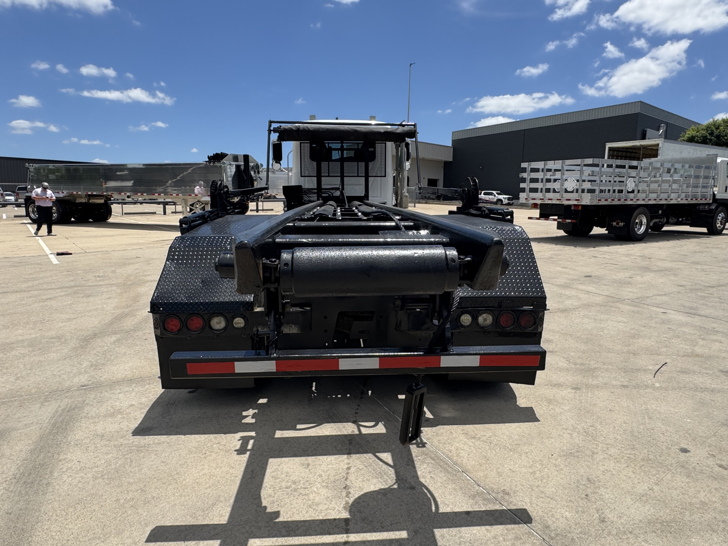 Rear view of a Mack GR64B roll-off truck showing bumper lights, hitch, and reflective striping.
