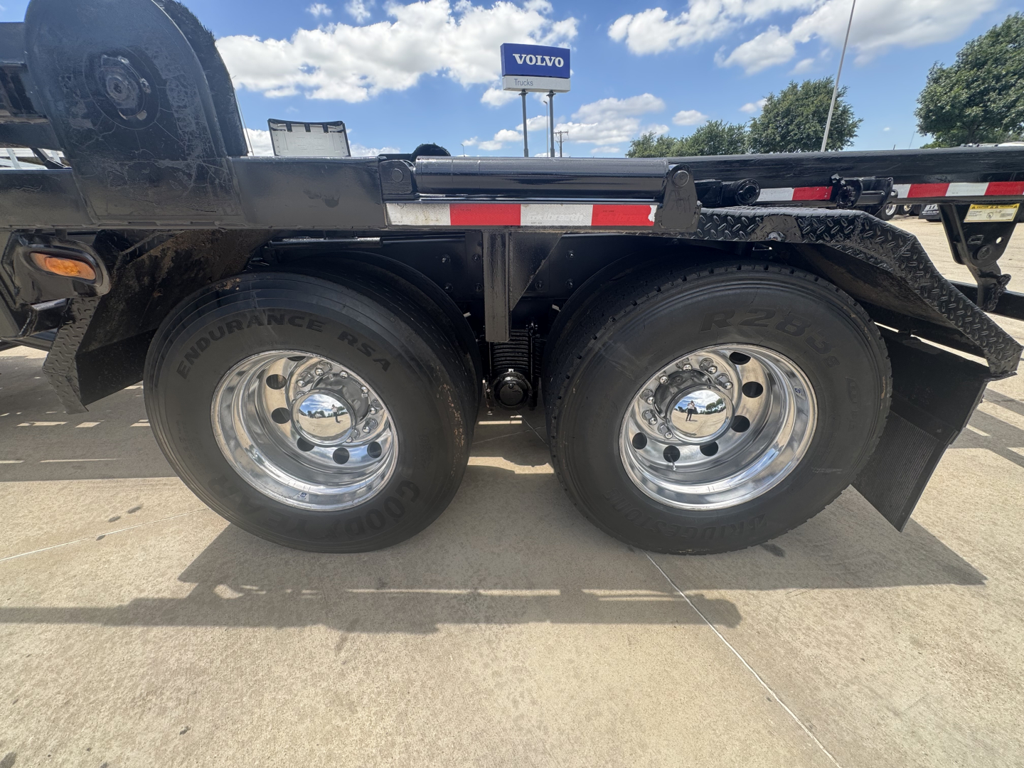 Dual rear wheel setup on a Mack GR64B roll-off truck showing tires, rims, and frame with mud flaps and side rail.