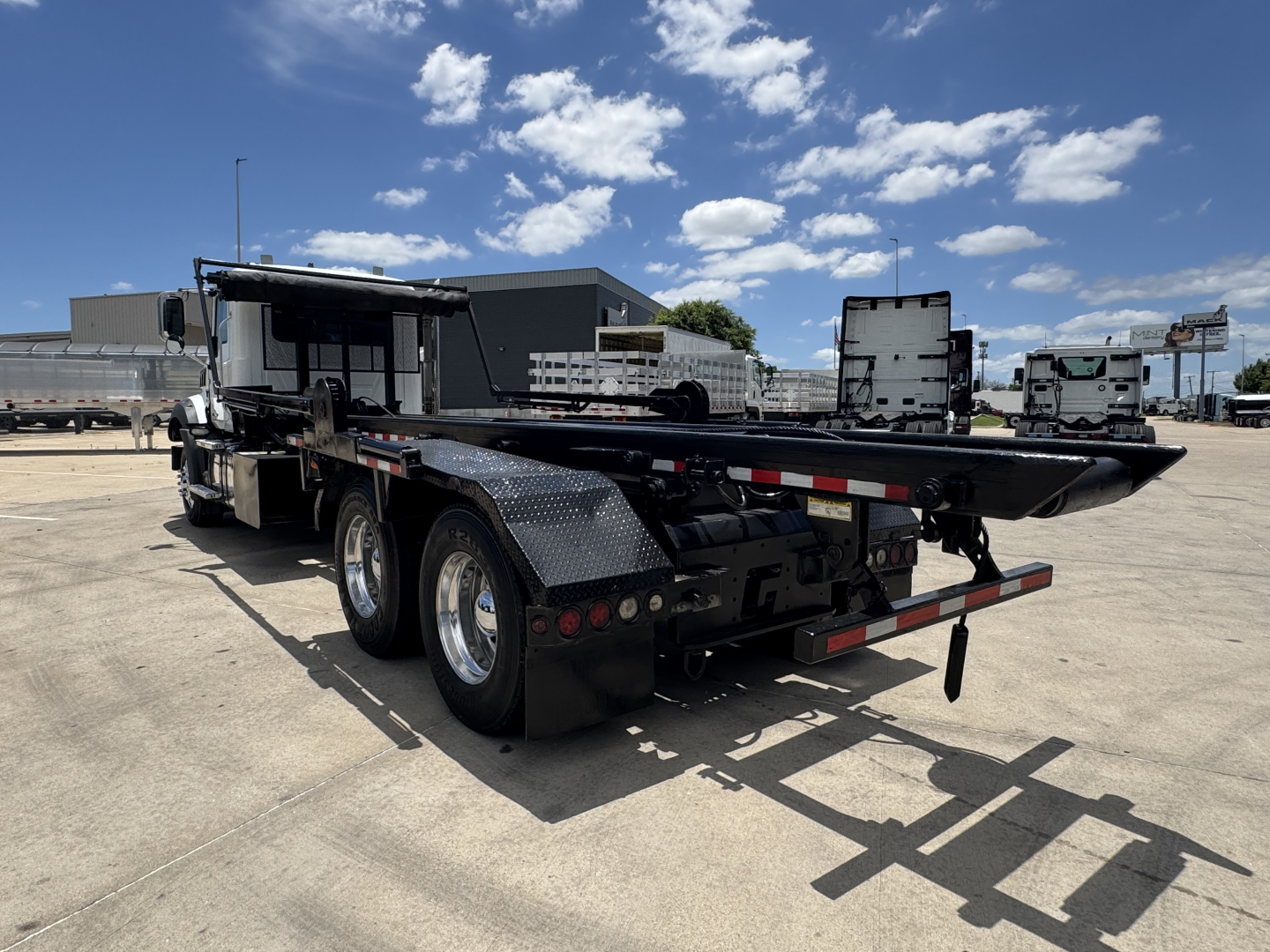 2023 Mack GR64B roll-off truck rear view showing dual rear axles, flatbed with storage, and black diamond-plate fenders.