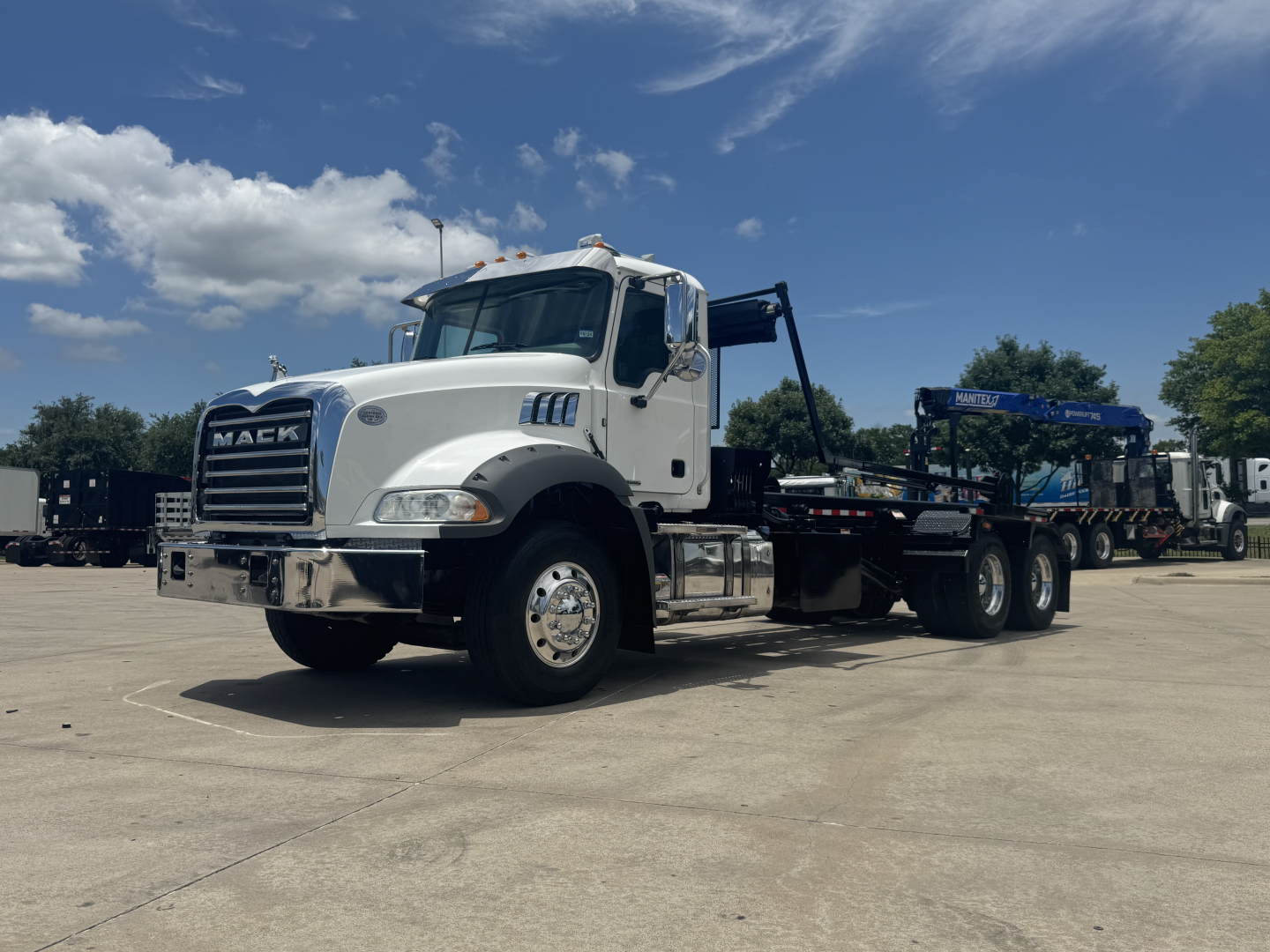 Mack GR64B rolloff truck in white cab showing front grille and chassis with flatbed and loading equipment