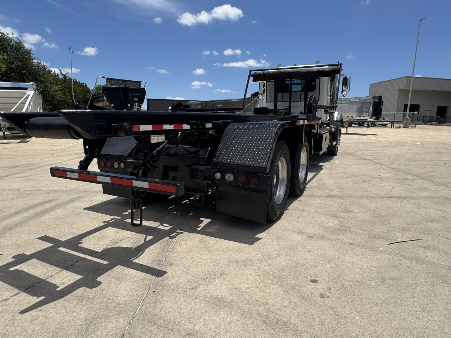 Mack GR64B rolloff truck rear view showing chassis and dual rear axles with black fenders and reflective safety strips.