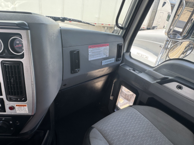 Cab interior of a 2023 Mack GR64B rolloff truck showing dashboard, steering wheel, driver door, and front passenger area with a warning label and vents.