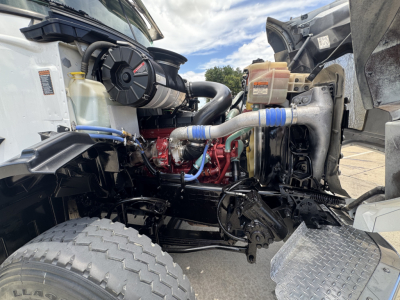 Mack GR64B engine bay showing intercooler hoses, coolant reservoir, hydraulic lines, and radiator with Komatsu-style cooling fan, front wheel and support frame visible.