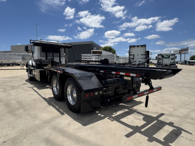 2023 Mack GR64B roll-off truck rear view showing dual rear axles, flatbed with storage, and black diamond-plate fenders.