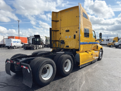 Tractor-trailer truck in a lot showing a bright yellow International LT625 sleeper cab with triple rear axles and mud flaps.