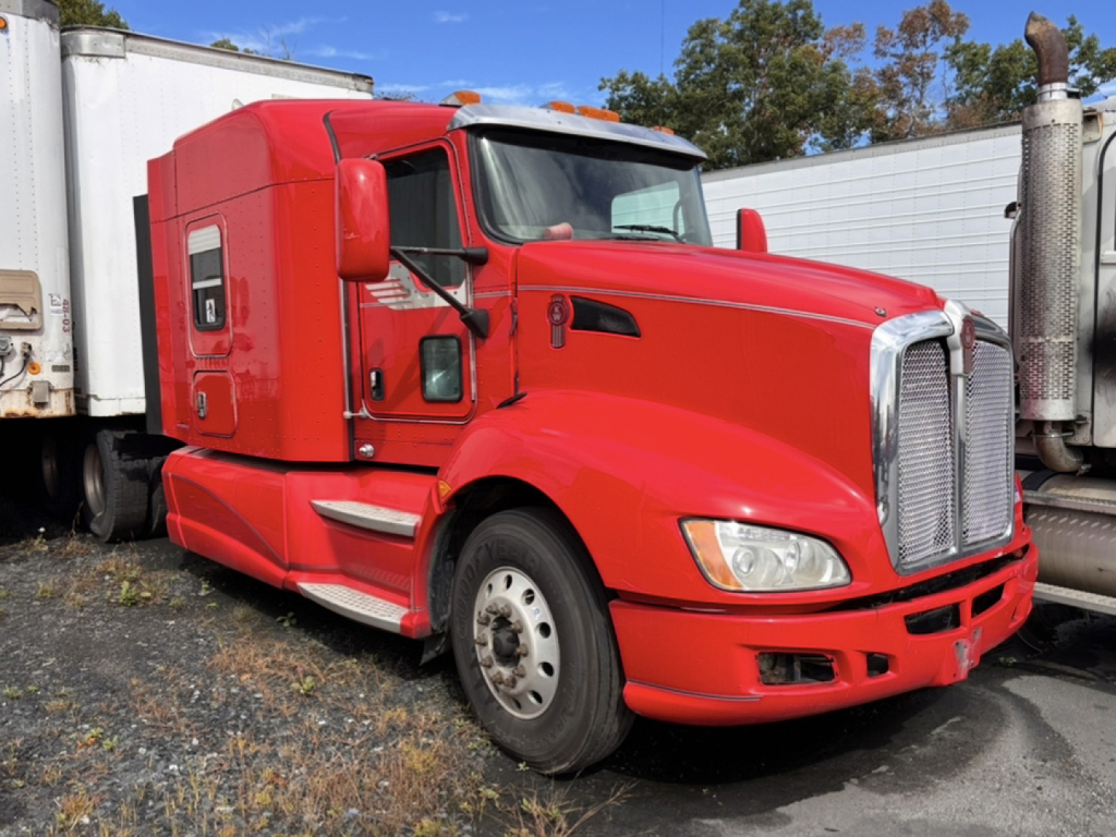 Red Kenworth T660 AeroCab semi-truck in a dealership lot. Front grille with chrome surround, large hood, two-tone headlamps, side mirrors, and aerodynamic cab with sleeper window.