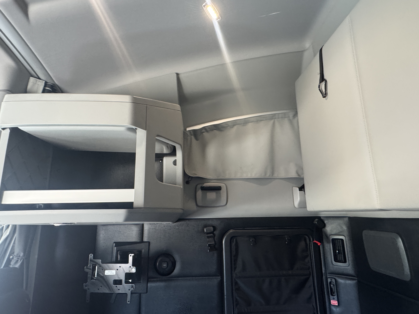 Kenworth T680 cab interior showing sleeper area with side storage drawer and fabric seat, interior paneling and overhead light.