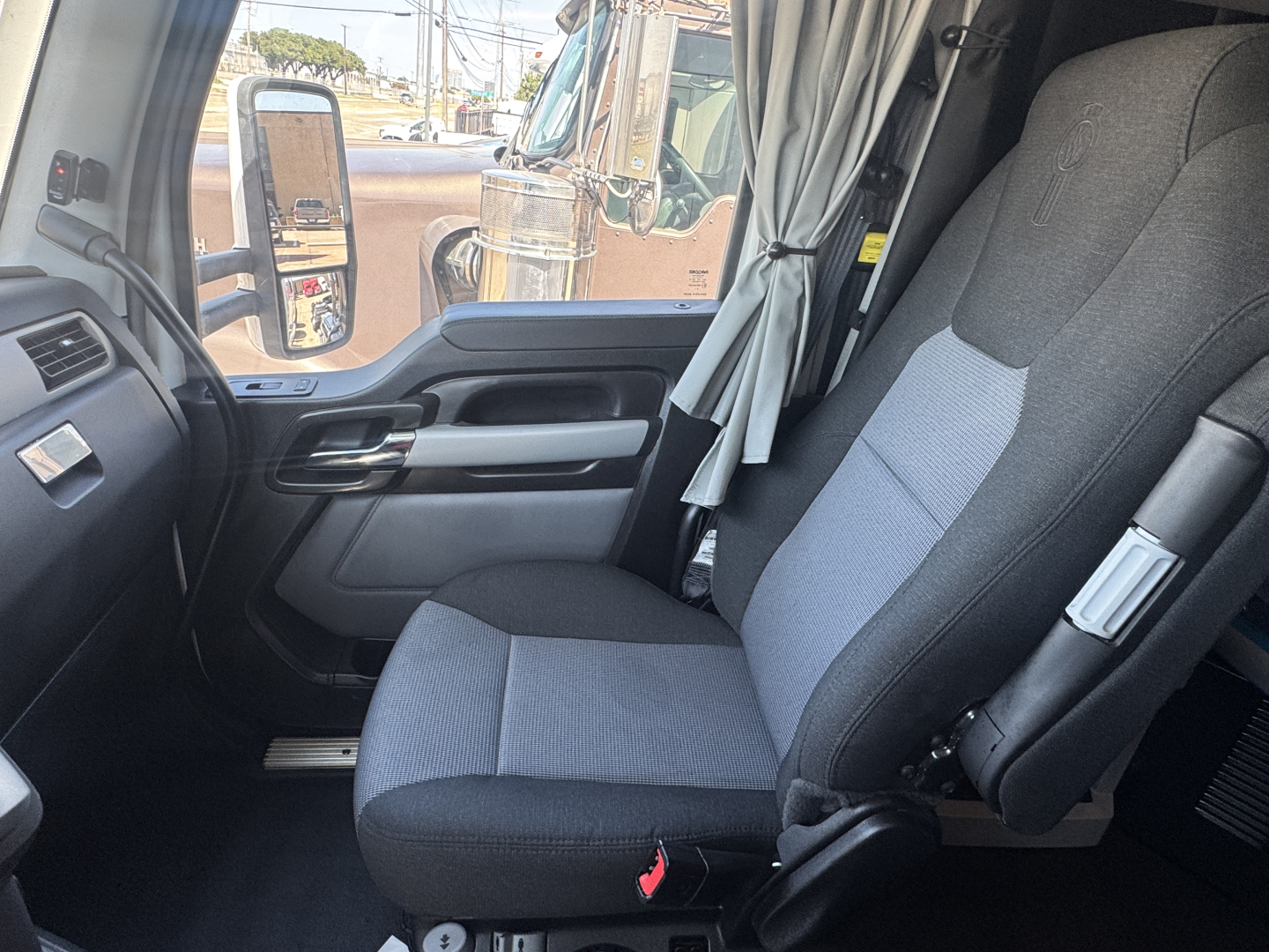 Truck cab interior with driver seat and door panel of Kenworth T680, gray fabric seats, window view and side mirror.