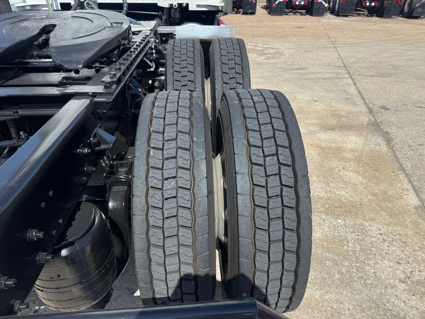 Kenworth T680 chassis showing dual rear drive tires and suspension components, with visible tire treads and part of the frame.