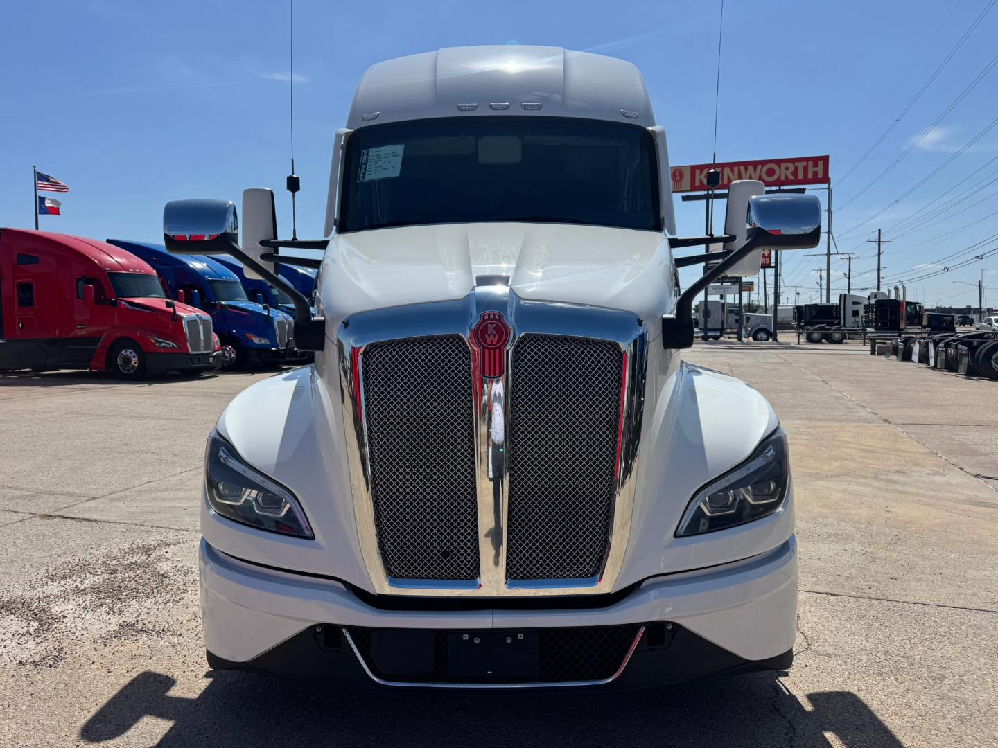 Kenworth T680 front view showing large vertical grille, chrome accents, headlights, and white cab in a truck dealership lot.