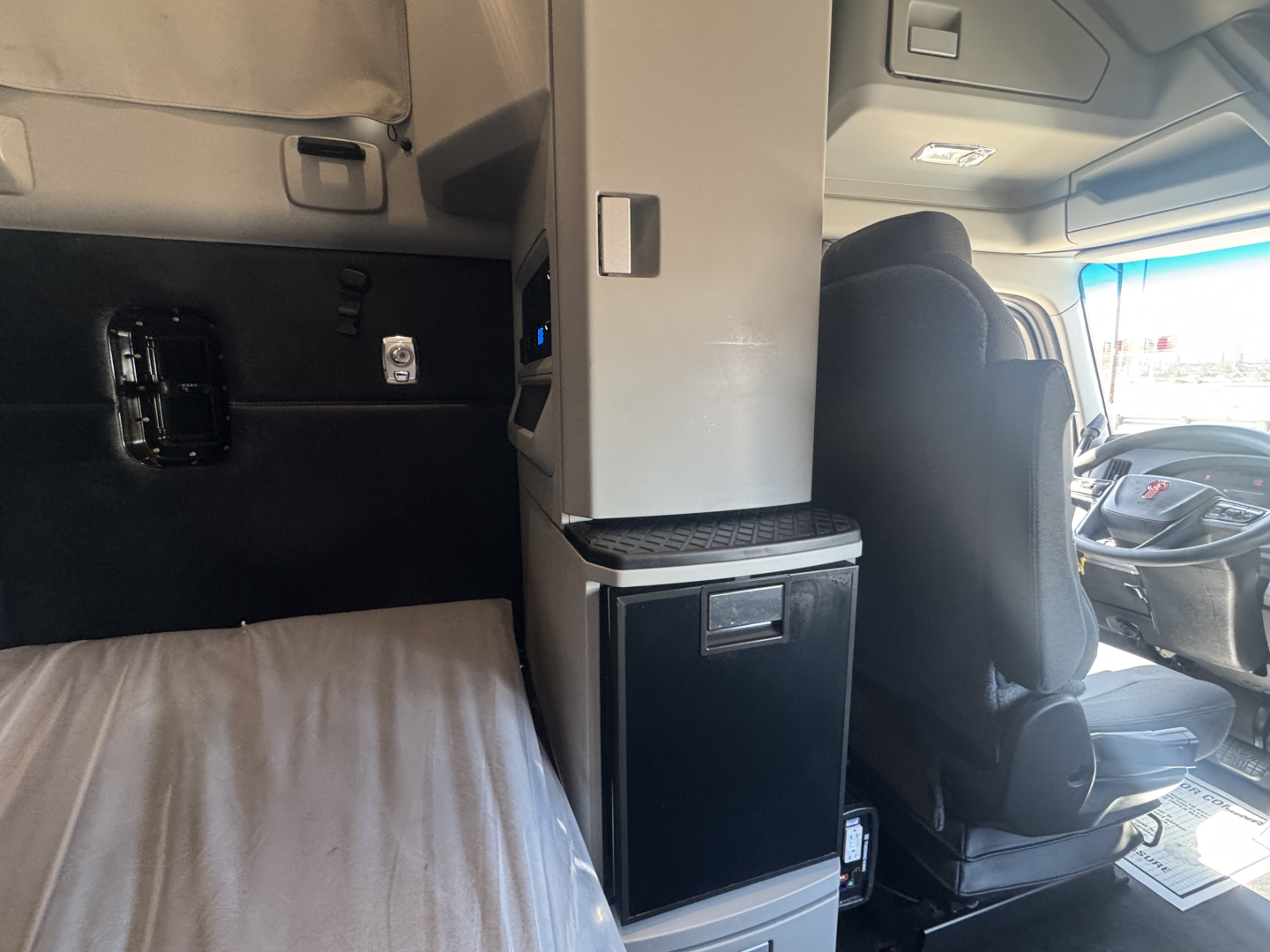 Kenworth T680 truck interior showing seat and partition with storage cabinet and small fridge.