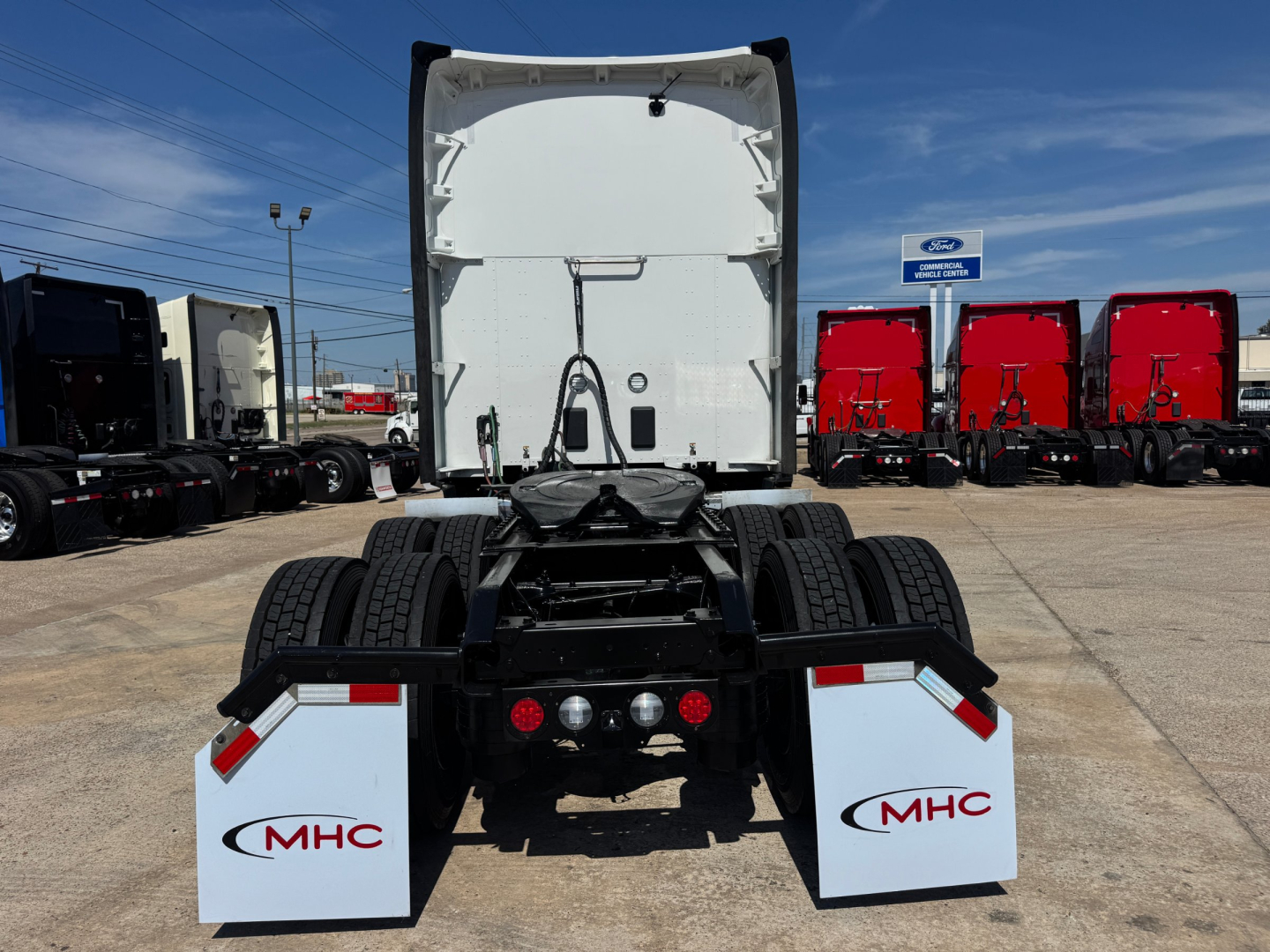 Rear view of a 2024 Kenworth T680 tractor chassis showing fifth wheel, rear lights, and mud flaps with MHC logos.