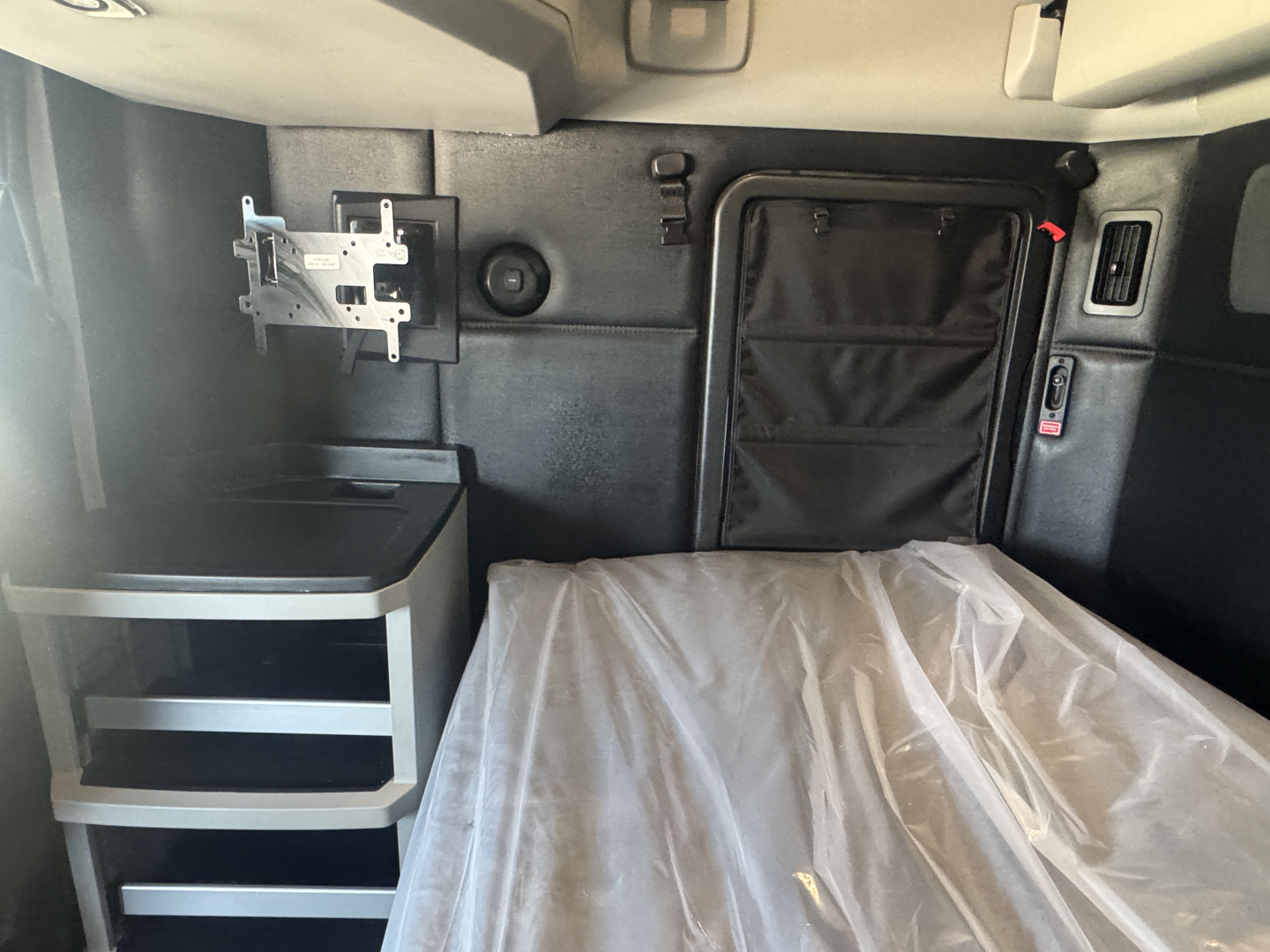 Kenworth T680 sleeper cab interior showing bed with plastic covering, storage pockets, and side panels.