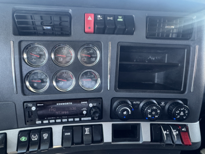 Kenworth T680 dashboard with six circular gauges, radio, and control switches; air vents and storage compartment visible.