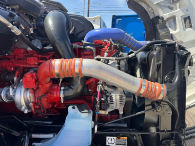 Kenworth T680 engine bay showing red engine block, silver exhaust pipe, and blue coolant hose in a used truck.