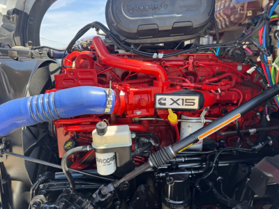 Kenworth T680 engine bay with red X15 engine, blue hose, coolant reservoir, and various lines; view from left side