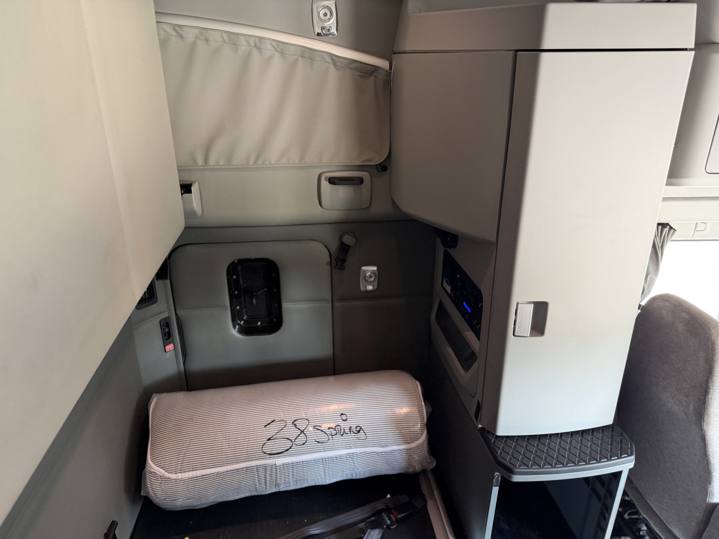 Truck cab interior showing sleeper area with a wrapped pillow and storage cabinets in a Kenworth T680 cab; no visible text aside from bed wrap.