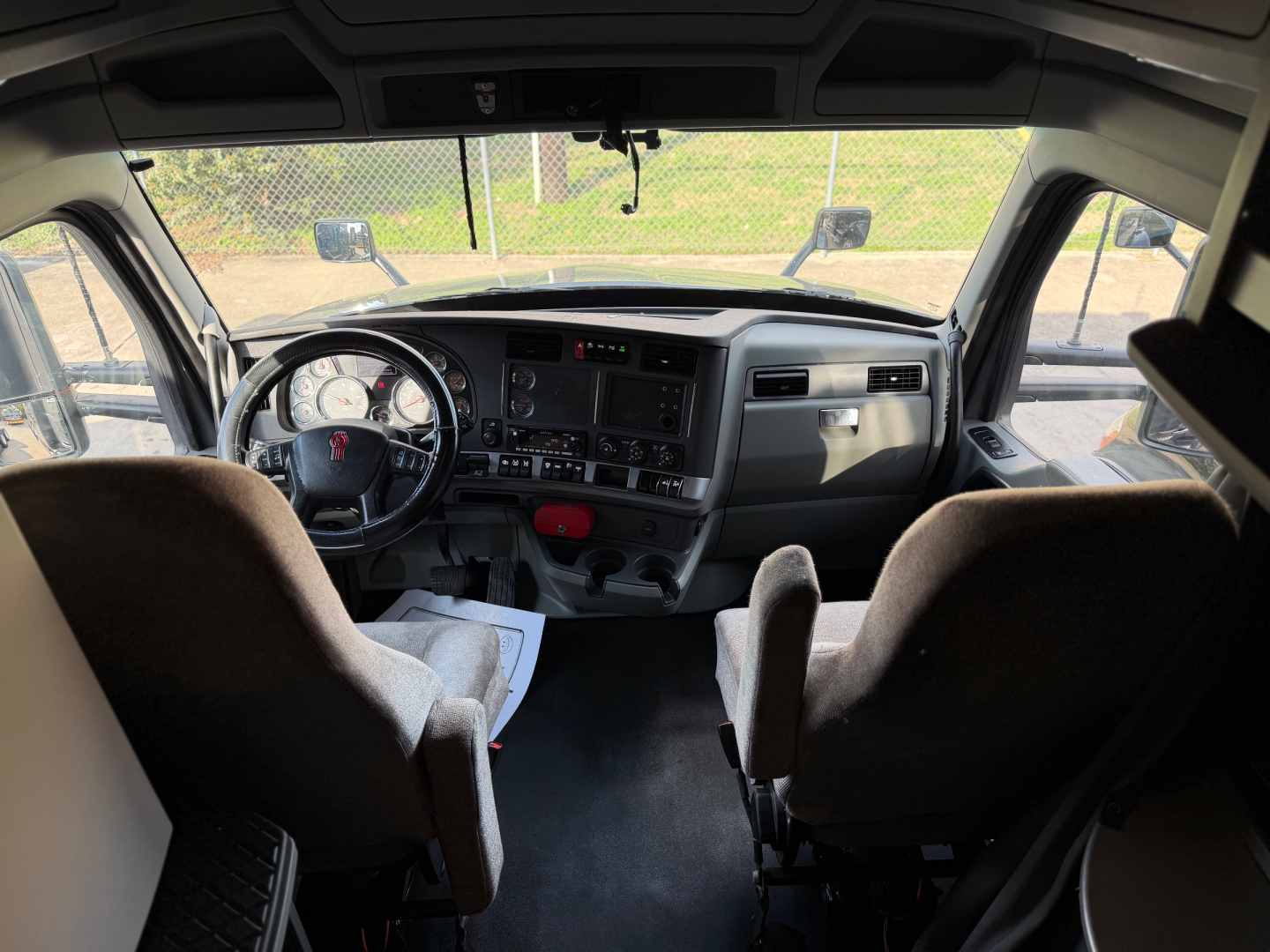 Interior cab view of a Kenworth T680 showing steering wheel, dashboard, and two seats, with controls and gauges visible.