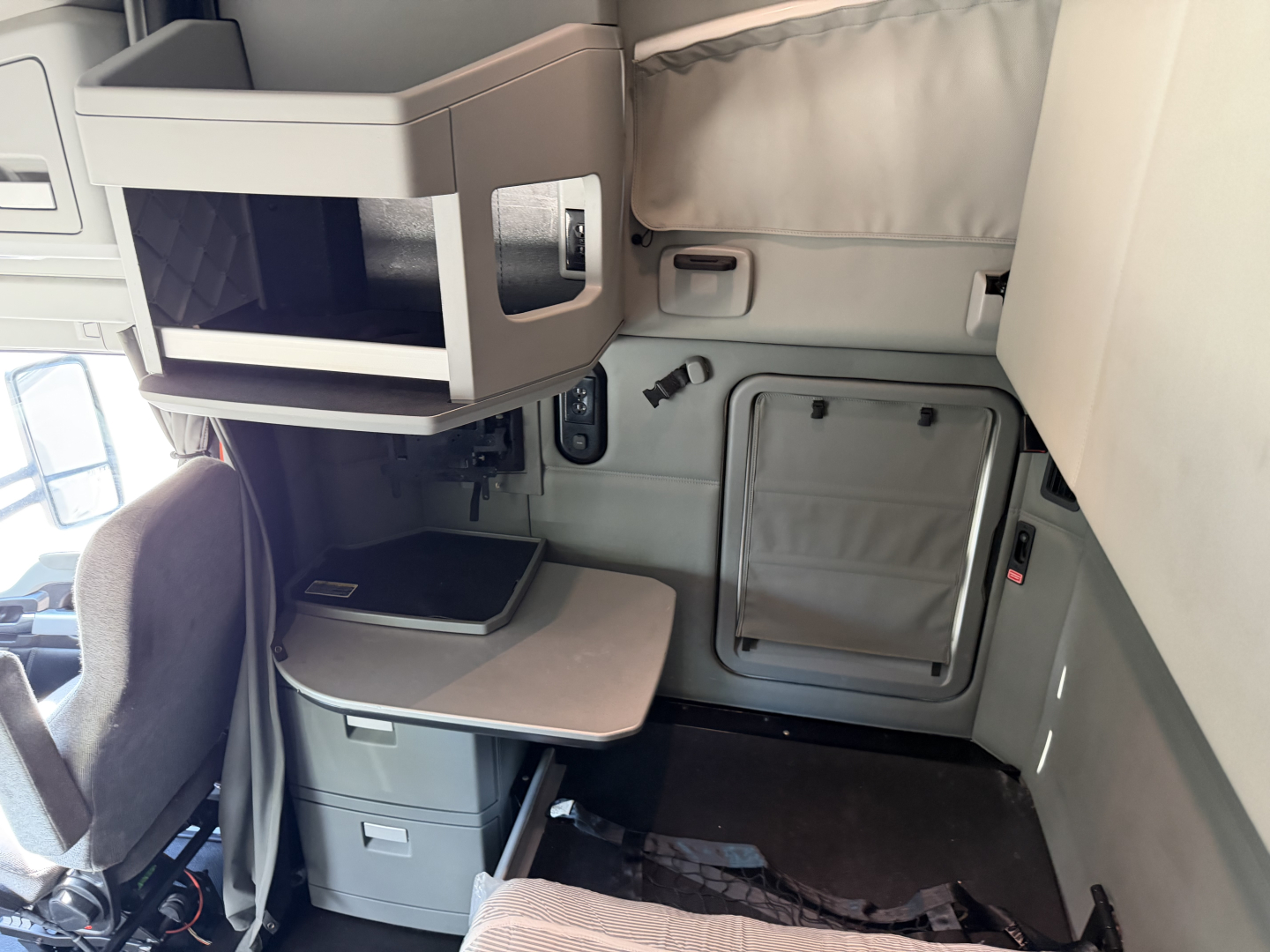 Kenworth T680 sleeper cab interior showing overhead bunk/cab storage, small desk, folded table, and side wall with access hatch.