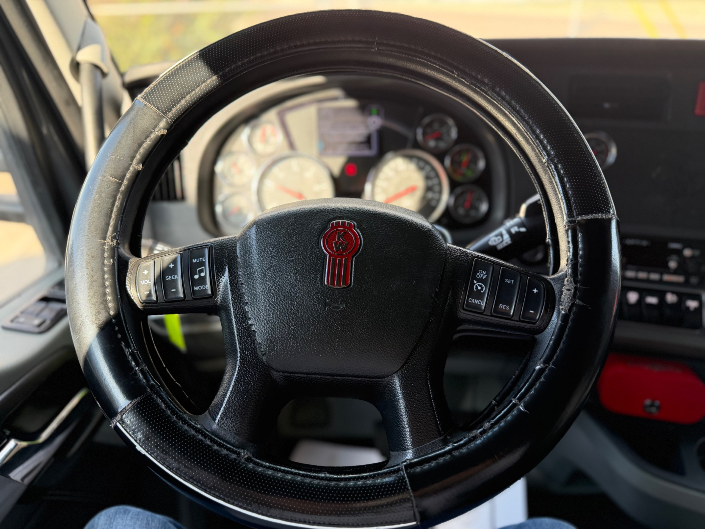 Steering wheel view from inside a 2022 Kenworth T680 showing the instrument cluster and steering wheel with Kenworth emblem.