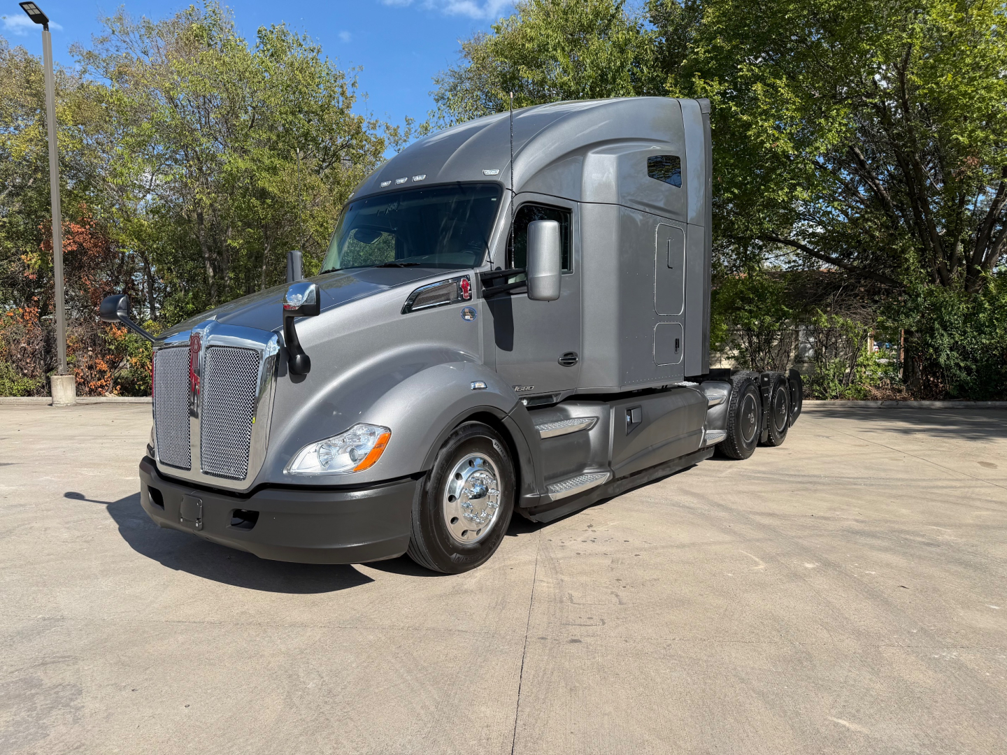 Kenworth T680 tractor in a parking lot, front-left view with dual rear axles and gray cab.