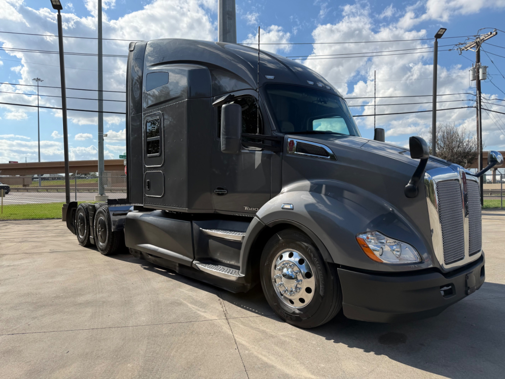 Kenworth T680 tractor in profile view showing sleeper cab, front grille, headlights, and chrome wheels; glossy gray paint and side mirror on a clear day.