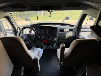 Dash and steering wheel of a Kenworth T680 truck cab with various switches, gauges, and a dashboard; two front seats with paperwork on floor.