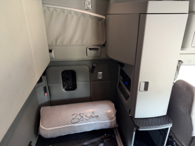 Truck cab interior showing sleeper area with a wrapped pillow and storage cabinets in a Kenworth T680 cab; no visible text aside from bed wrap.