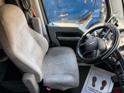 Kenworth T680 cabin with steering wheel and gray fabric seat, dashboard controls visible.