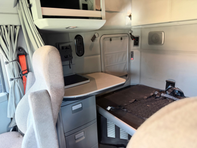 Kenworth T680 sleeper cab interior showing side table, storage drawers, bunk bed area, and seating in view.