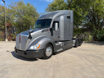 Kenworth T680 tractor in a parking lot, front-left view with dual rear axles and gray cab.