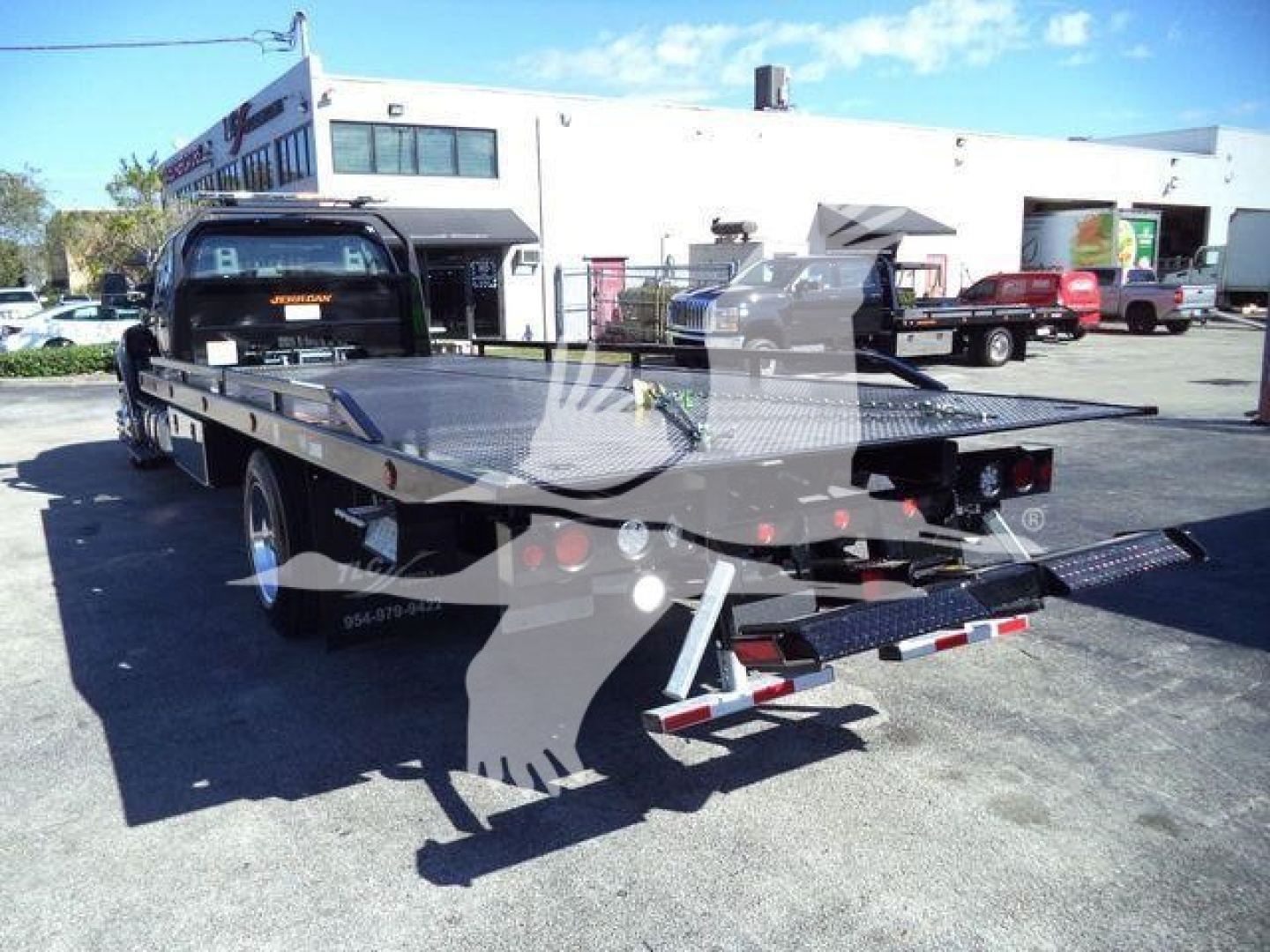 Flatbed tow truck with a steel rollback bed in a dealership lot; rear view showing ramps and towing equipment, Ford F-750 chassis visible