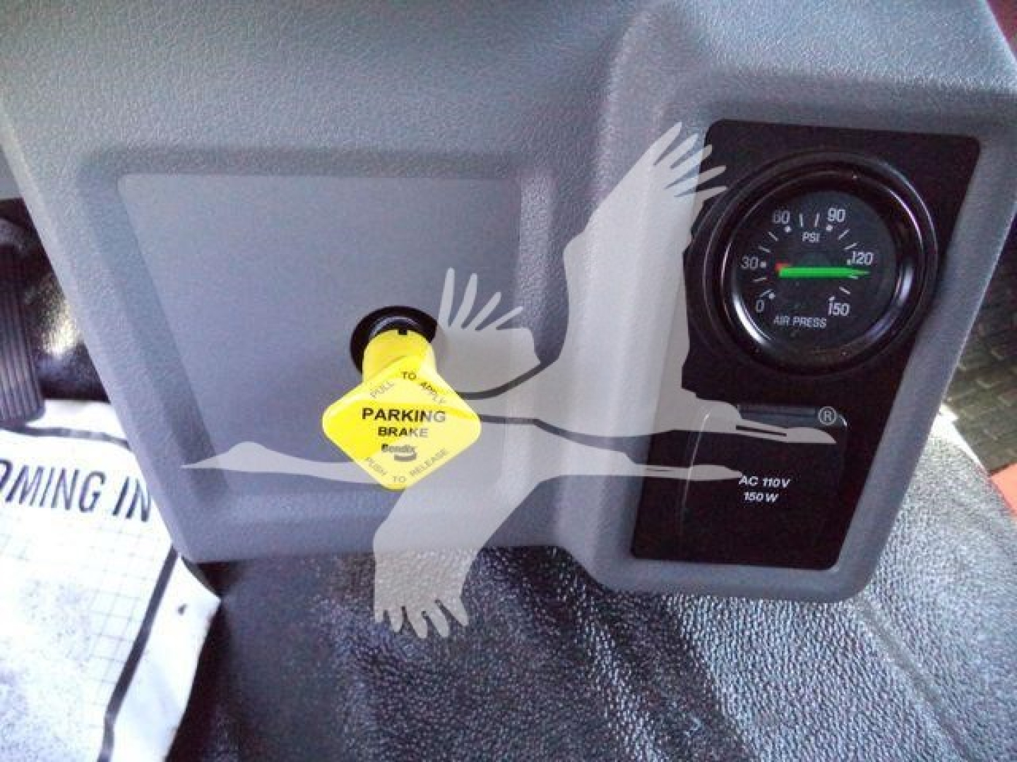 Dashboard area of a 2024 Ford F750 rollback showing parking brake knob and a pressure gauge; yellow parking brake warning cap visible.
