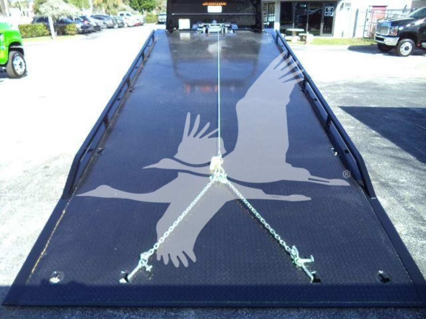 Ford F-750 rollback bed viewed from rear showing ramp bed with chain attachments and bird watermark reflection