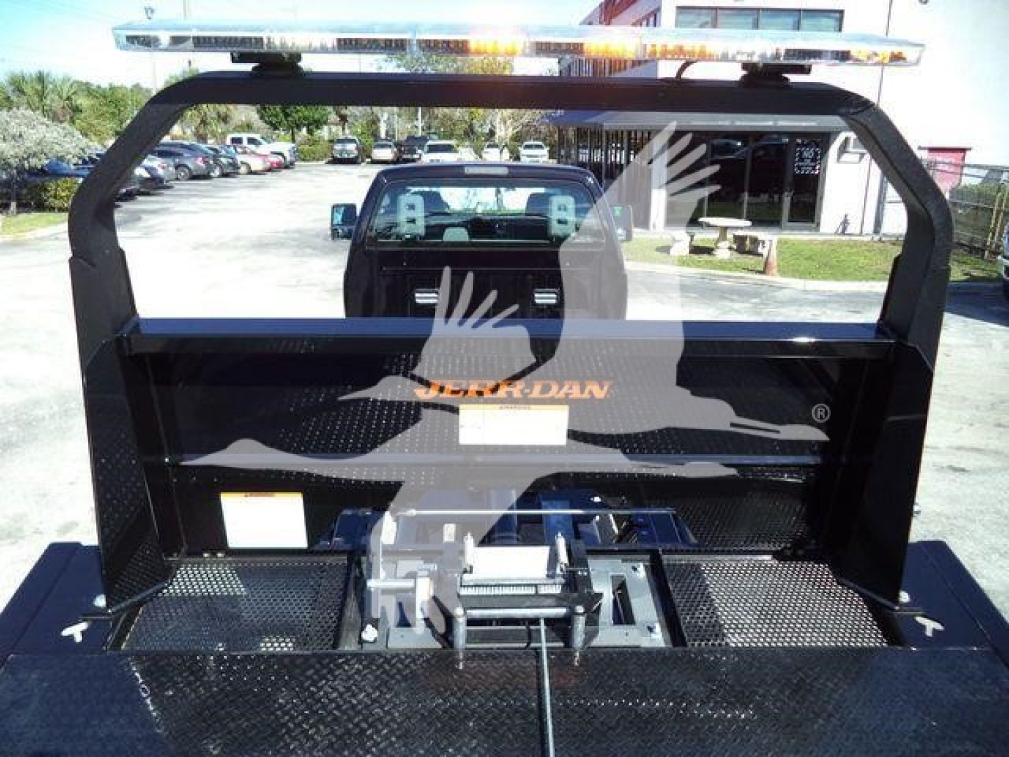 Truck bed with rollback equipment and elevated light bar, rear view through cab showing aluminum hitch and mounting hardware.