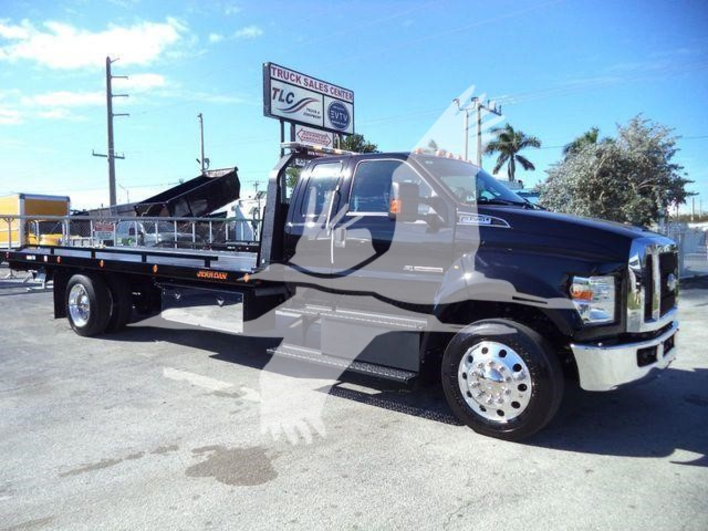 Ford F750 tow truck with rollback bed, side view showing cab, flatbed and chrome dual rear wheels.