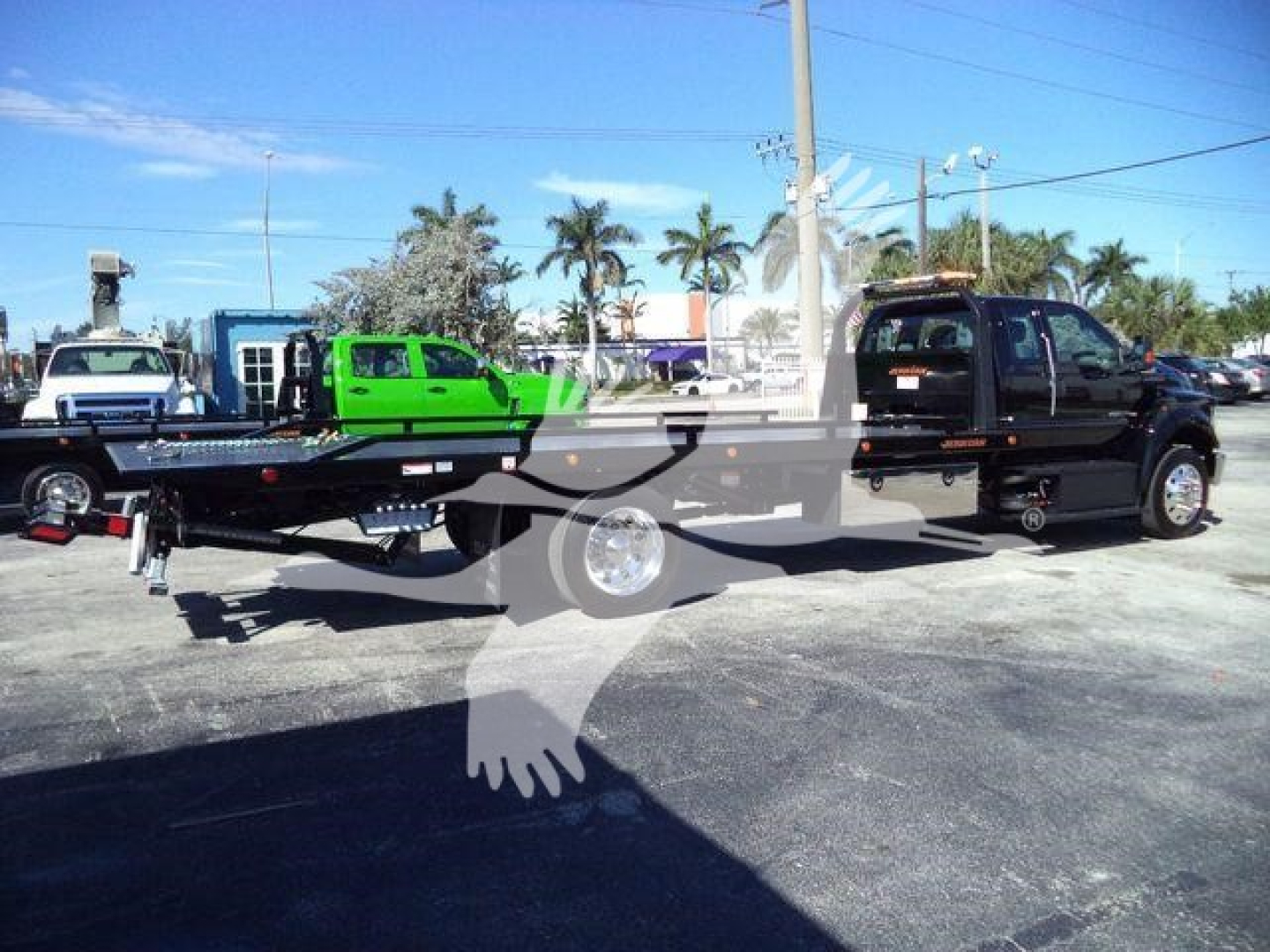 Truck bed tow truck machine on a rollback with a black cab and long flatbed, with a green vehicle on the bed.