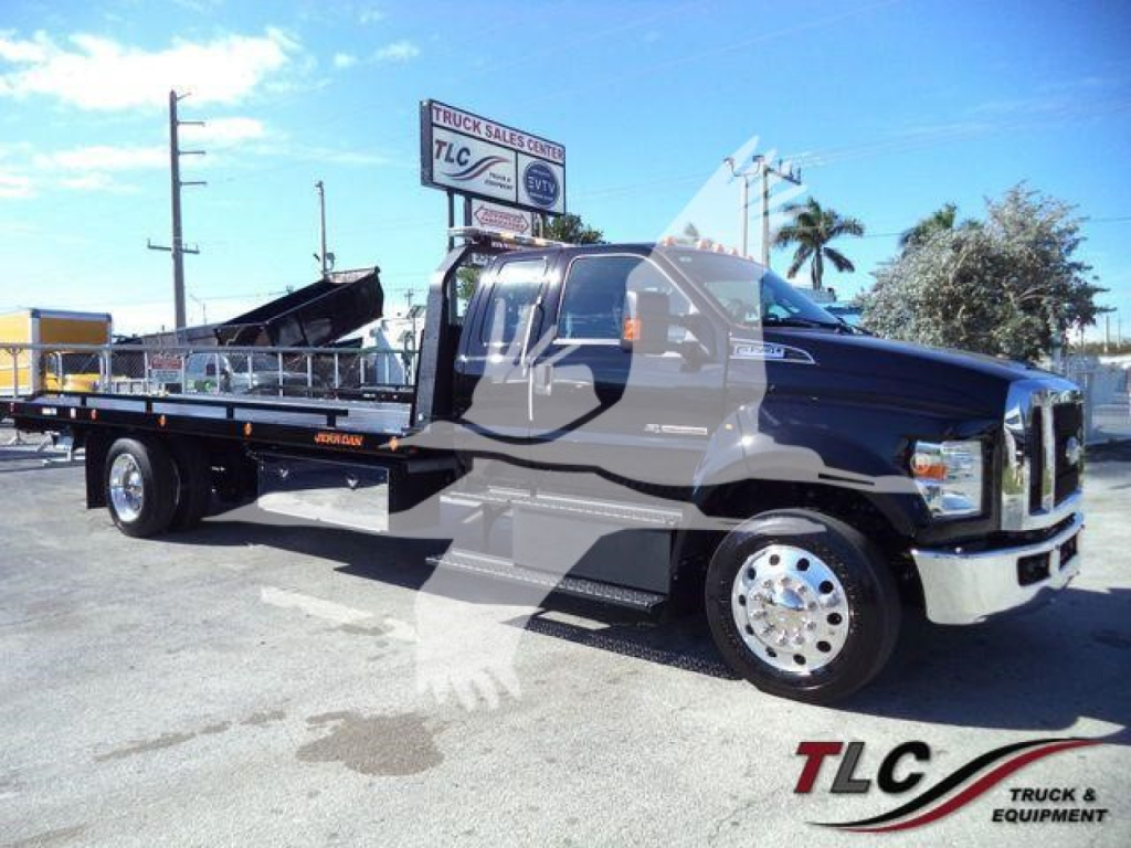 Ford F-750 rollback truck in blue with flatbed and hydraulic towing gear, side view showing cab, front grille, chrome wheels, and callouts from TLC Truck & Equipment.