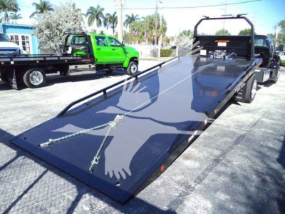 Ford F-750 rollback tow truck with a long tilt bed in lowered position, chains and hooks visible, black metal rails along bed edges.