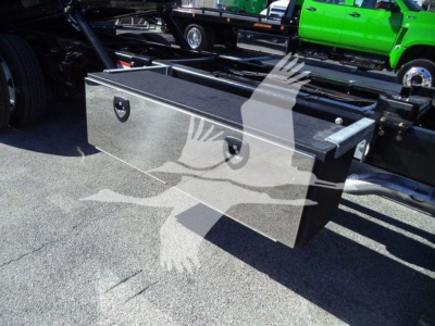 Toolbox mounted under truck bed with secure latches and chrome finish; hydraulic lines and chassis visible in background.