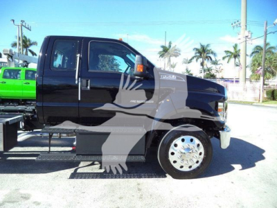 Ford F750 rollback truck side view showing cab and chassis with black paint, white wheel rims, and steps. visible text includes 'F-750' on the door and 'FORD' emblem on grille, with side mirrors and orange marker lights.