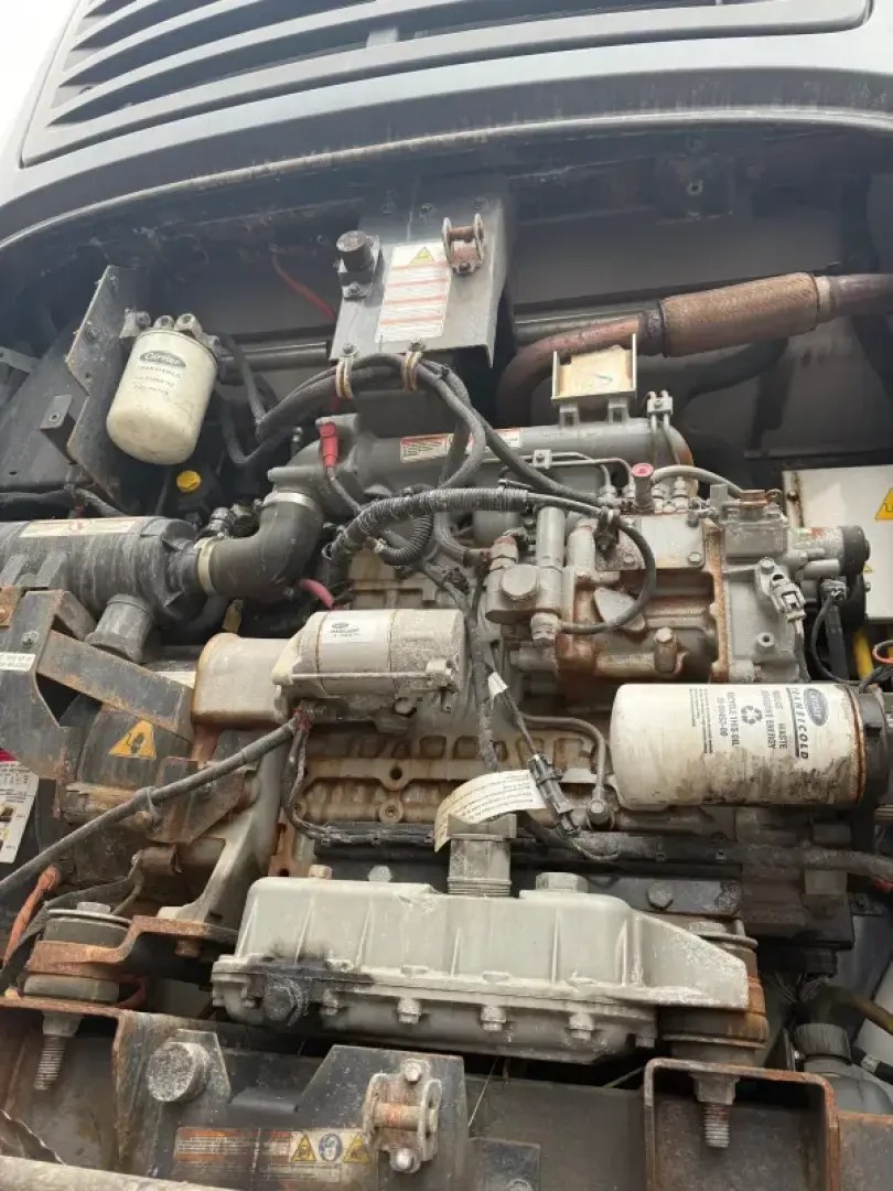 Refrigerated trailer engine bay showing diesel engine components, hoses, and electrical wiring with label stickers and a white cylindrical filter.