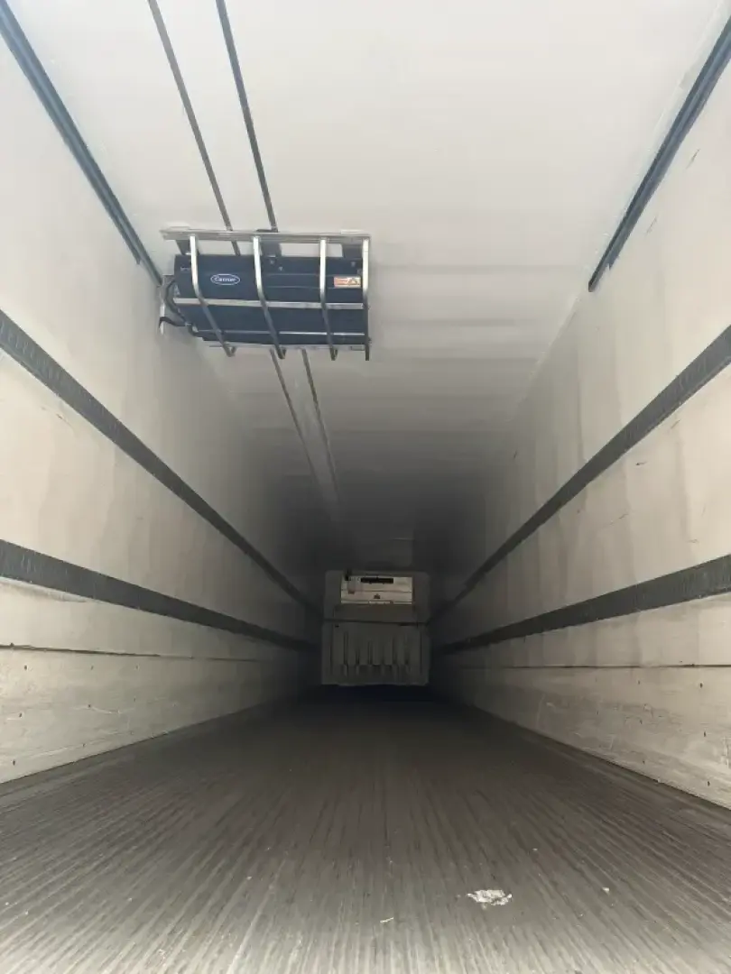 Inside a refrigerated trailer with a load platform near the ceiling and a truck overhang in the distance, showing the long, empty cargo area.